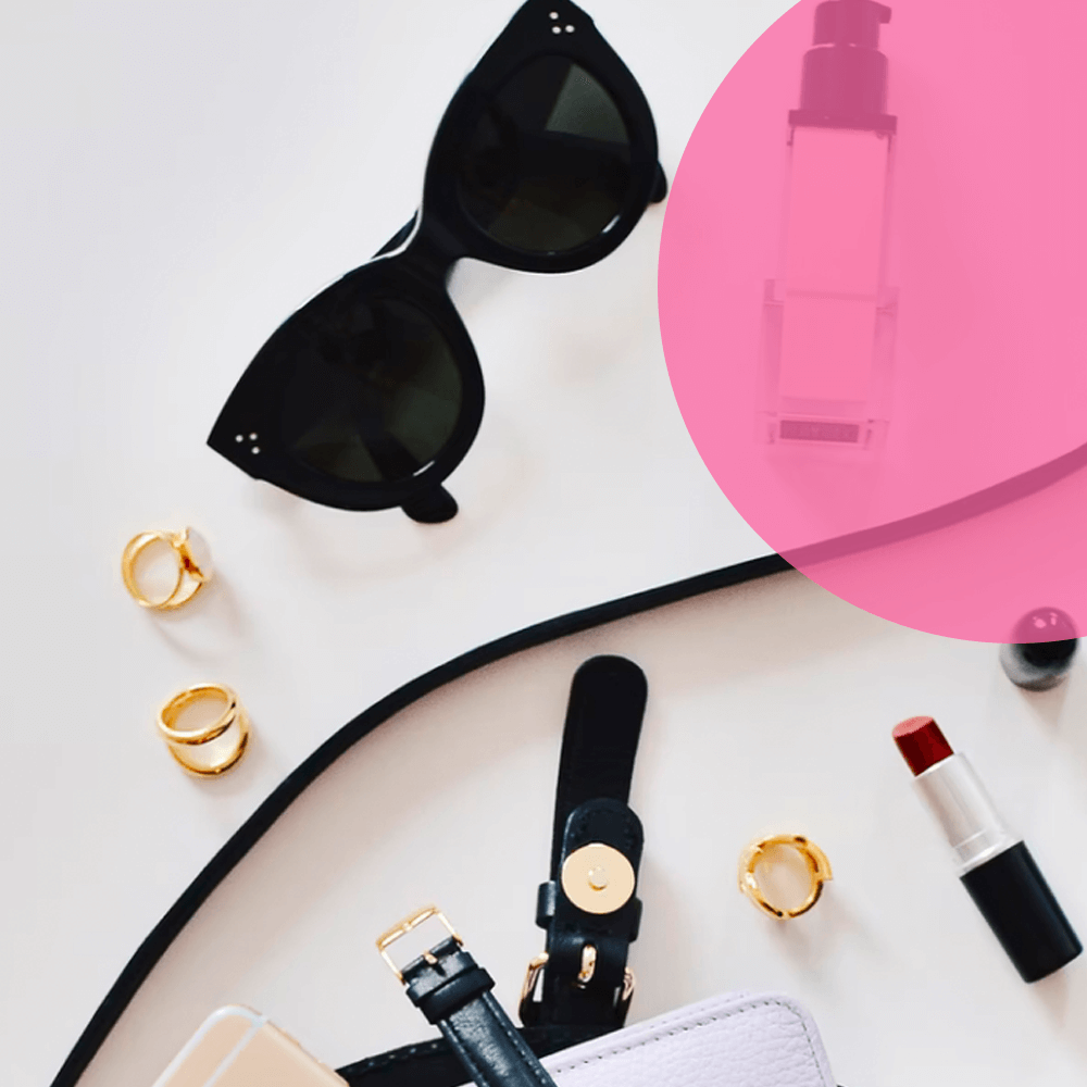 Sunglasses, jewellery and beauty products arranged on a pink and white background